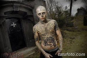 Фото тату: мужчина с татуировками в стиле биомеханика и хоррор позирует на фоне старого кладбища, создавая мрачную и загадочную атмосферу.